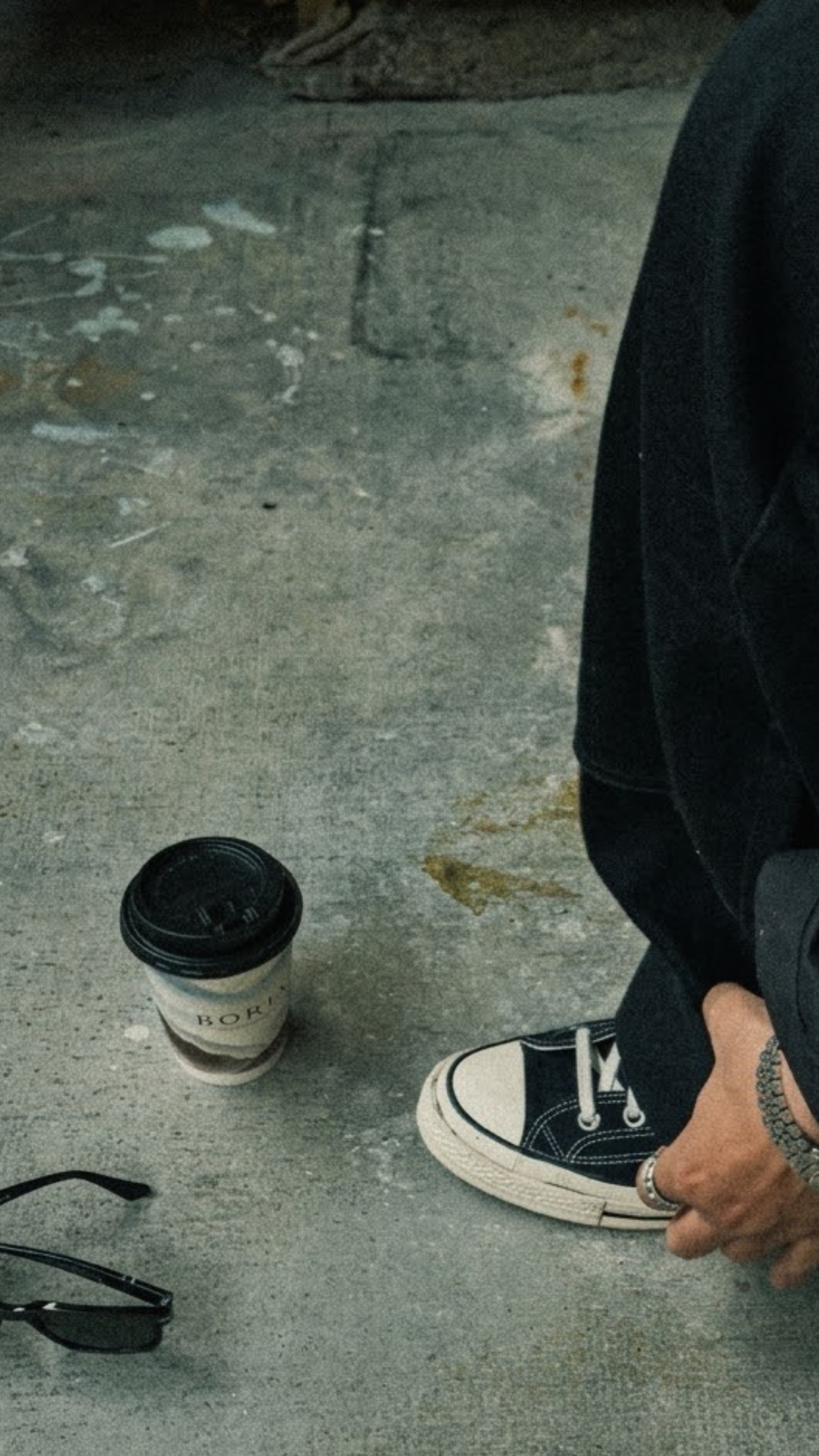 A BORIA cup on the pavement beside a person in black and white sneakers